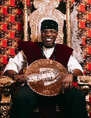 Theo seated on an ornate gold throne in a red and black outfit